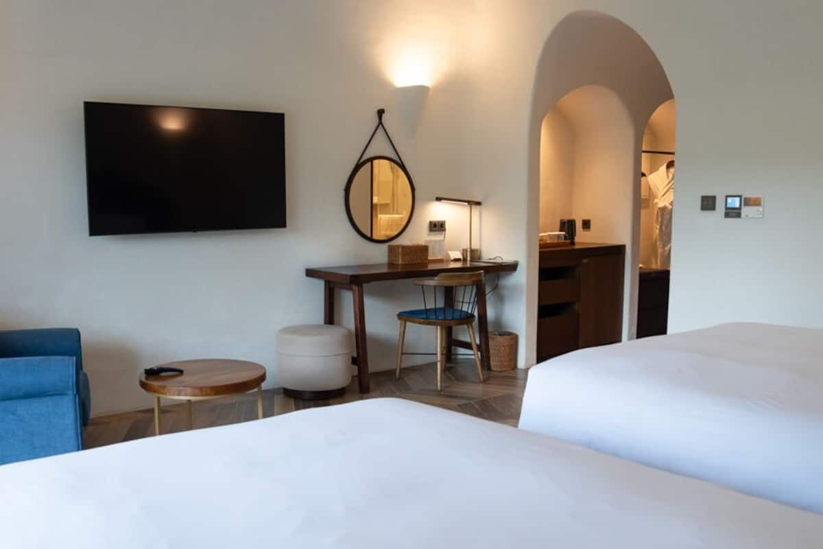 A hotel room with two beds, a desk with a chair, a TV, and a mirror.