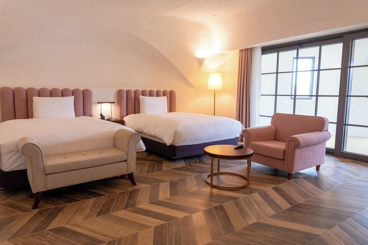 A hotel room with two beds, a sofa, a small table, and a large window.