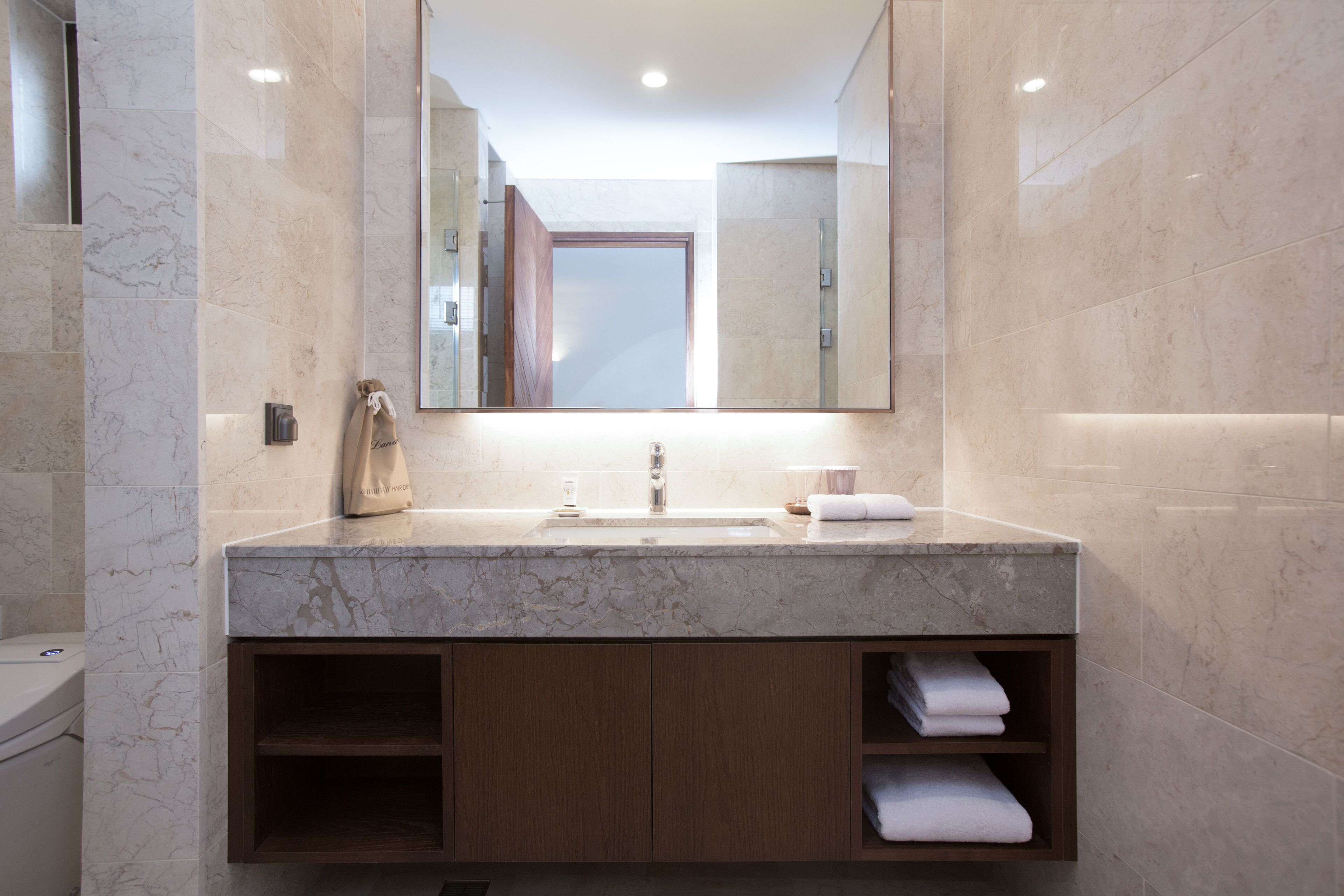 A modern bathroom with a marble sink, wooden cabinets, and a large mirror.