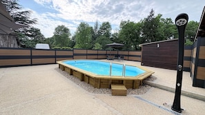 Una piscina de madera rectangular con una escalera, rodeada por un patio de grava y una valla de madera.