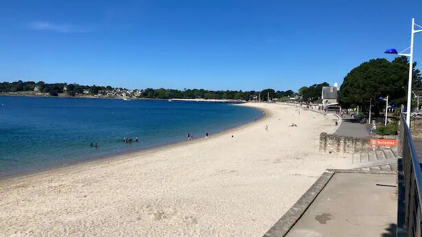 En strand med blå himmel, sand og et par personer.