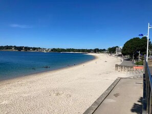 Een strand met een helderblauwe lucht, een zandstrand en enkele mensen.