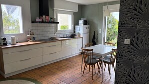 Et kompakt køkken med en central ø, et spiseområde med fire stole, et køleskab og en mikrobølgeovn.