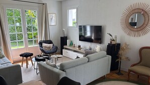 En stue med sofa, lænestol, fjernsyn og spiseplads med bord.
