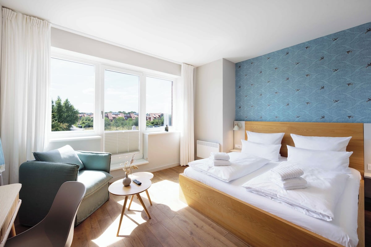 Une chambre d’hôtel avec un grand lit, un canapé, une petite table et une vue sur la ville grâce à de grandes fenêtres.