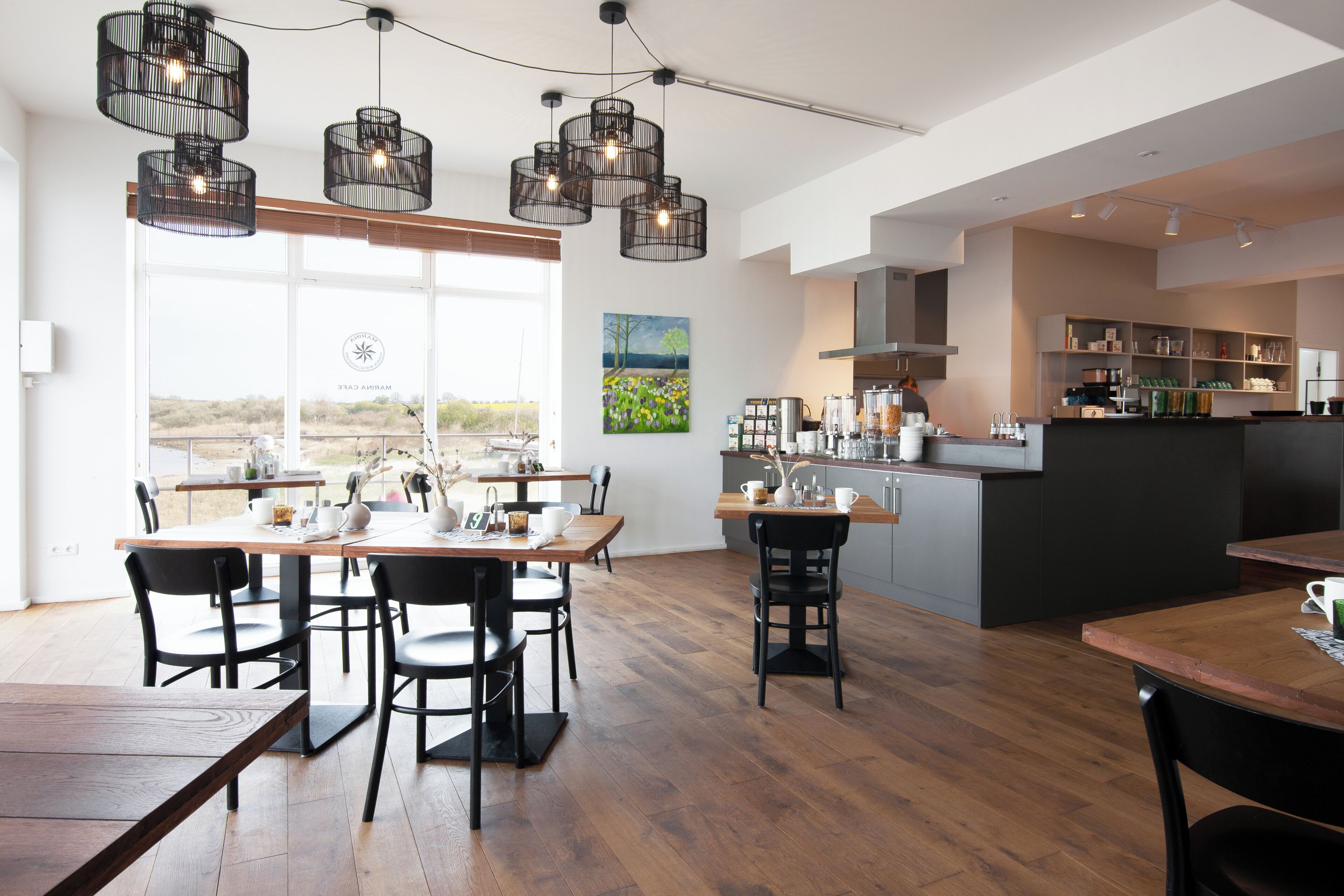 A modern café with wooden tables and chairs, a bar area, and a large window offering a view.