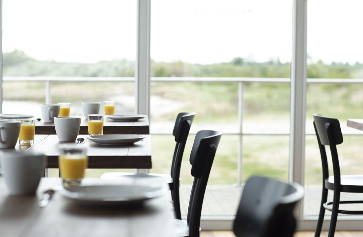 A dining table with breakfast items and chairs, large windows with a view of greenery.