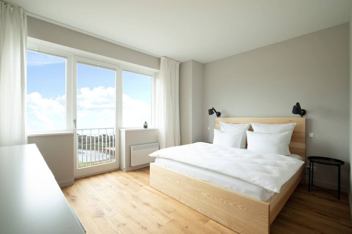 Une chambre avec un grand lit, une fenêtre avec des rideaux, un radiateur et une petite table.