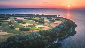 An aerial view of a golf course with a body of water on one side and a forested area on the other.