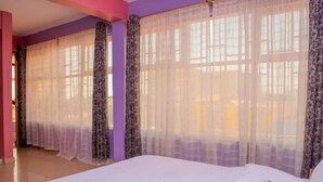 A bedroom with a large bed, purple walls, and sheer curtains. - The Trumpet Inn (Nyeri)