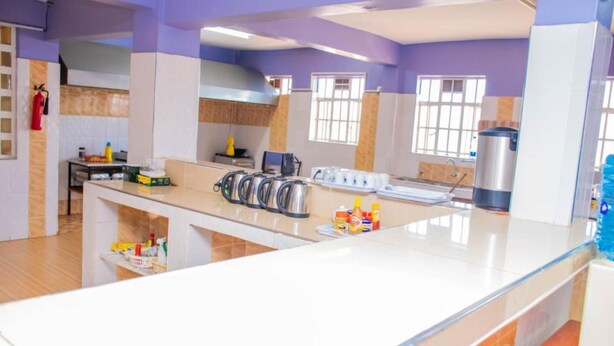 A modern kitchen with a central island, stainless steel appliances, and a window providing natural light. - The Trumpet Inn (Nyeri)