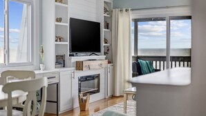 Uma sala de estar moderna com televisão de tela plana, armários brancos e uma grande janela com vista para o mar.