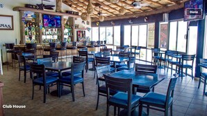 Een restaurant met meerdere tafels en stoelen, een bar met diverse flessen en een televisiescherm.