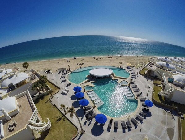 Ein Resort mit einem zentralen Schwimmbad, Liegestühlen und einem Strandbereich.