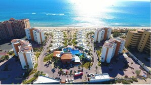 Een resort met meerdere hoge gebouwen, een centraal gelegen zwembad en uitzicht op het strand.