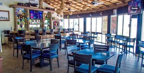 Een restaurant met meerdere tafels en stoelen, een bar met diverse flessen en een televisiescherm.