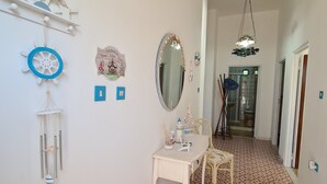 A hallway with a patterned floor, a white desk with chairs, a mirror, and wall decorations including a welcome sign and a blue circular object. - Villa AURORA, beautiful sea view! 400mt from the sandy beach. (Lizzano)