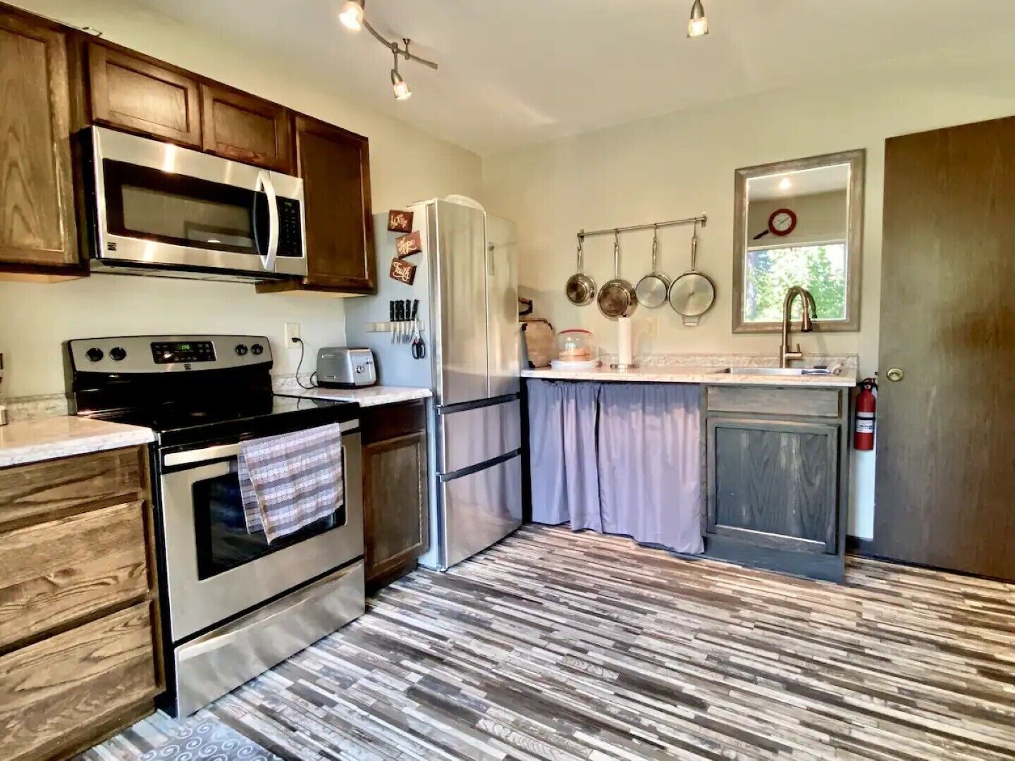 A compact kitchen with wooden cabinets, stainless steel appliances, and a tiled floor.