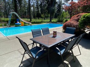 A poolside area with a table and chairs, a slide, and a well-maintained lawn. - CdA Hotspot - Hot Tub, Pool, & Sauna (Coeur d Alene)