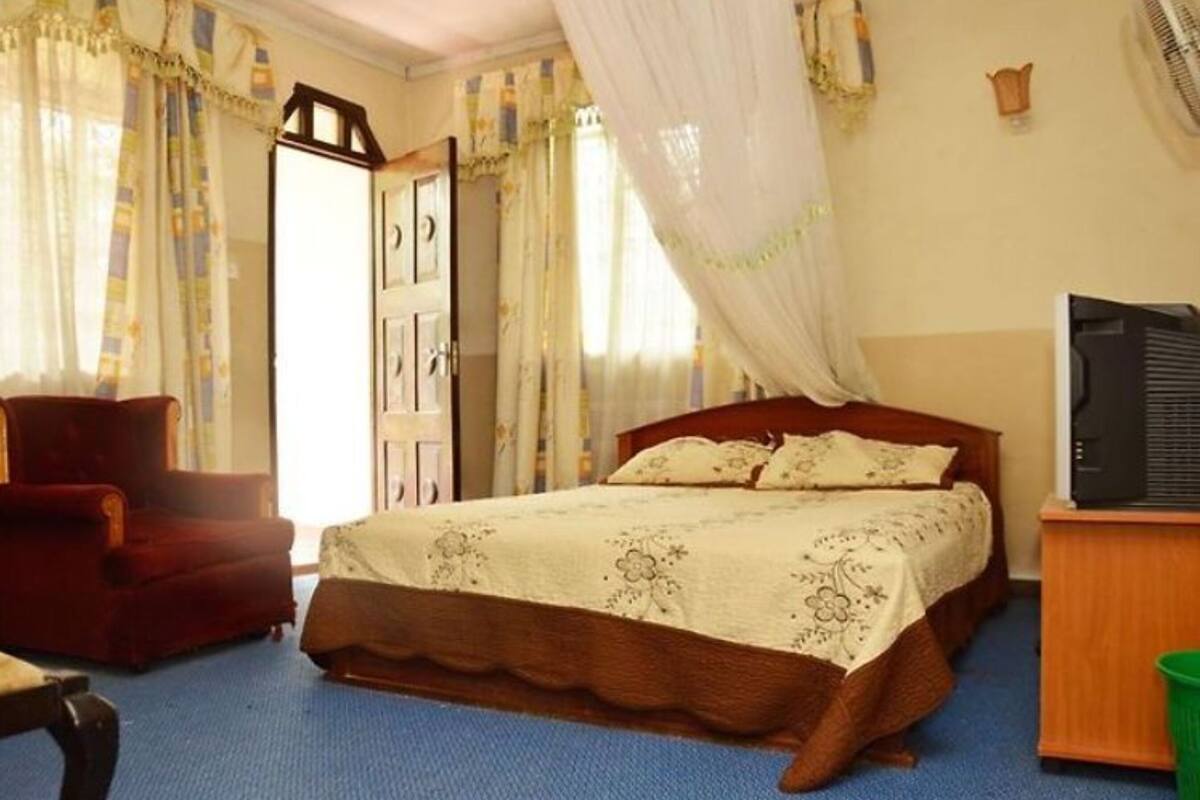 A bedroom with a wooden bed, a red armchair, a television, and curtains.