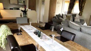 Un coin repas avec une table en bois dressée pour quatre personnes, un canapé gris et une cuisine en arrière-plan.