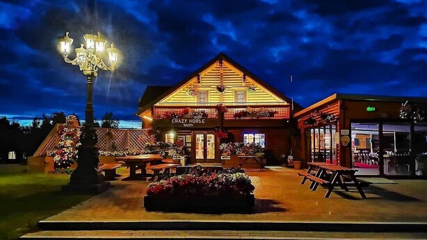 Un bâtiment rustique, agrémenté d’une enseigne indiquant « Crazy Horse Saloon », avec une façade en bois, des places assises en plein air et un lampadaire décoratif.