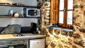 A rustic kitchen with stone walls, wooden beams, a microwave, a coffee maker, and a small refrigerator. - Former "U FRAGNU" wine press (Omessa)