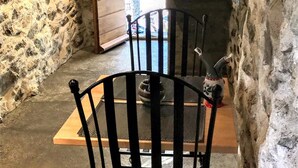 A stone-walled room with a wooden door leading outside. A black metal chair is positioned in the center. - Former "U FRAGNU" wine press (Omessa)