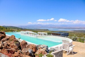 A pool with a view of the sea and mountains, surrounded by rocks and white chairs. - Lemon Valley Farm (Nakuru)
