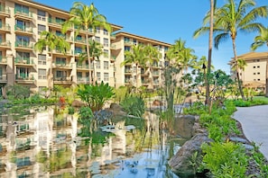 Relax by the pool surrounded by lush greenery and palm trees, with a soothing waterfall nearby.