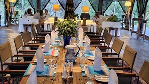 Un área de comedor cubierta con carpas, mesas dispuestas para una comida, rodeada de sillas y lámparas.
