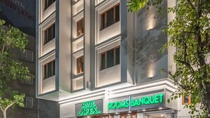 Un hôtel doté d’une façade moderne, d’une entrée bien visible et d’une enseigne indiquant « Hôtel Apex » et « Salles de réception ».