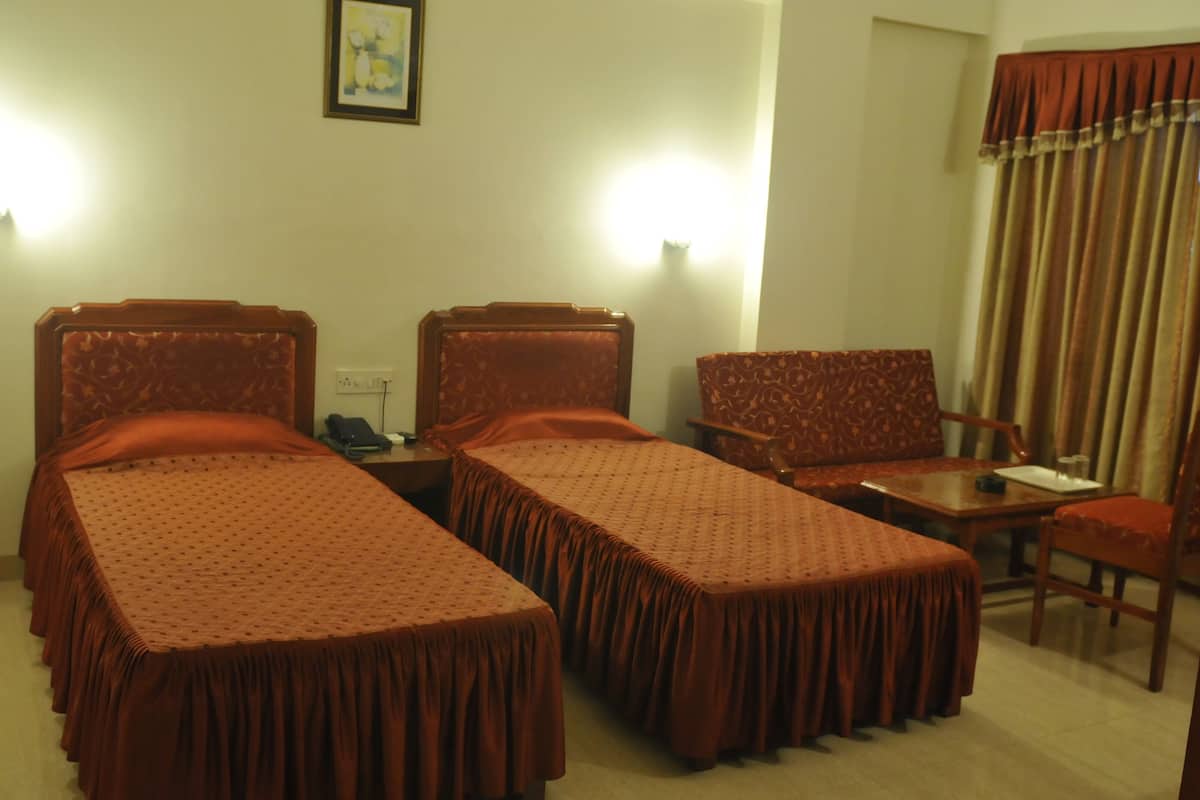 A hotel room with two single beds, a small table, a chair, and a desk.