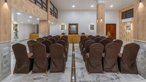 Une salle de conférence avec des rangées de chaises marron, une longue table et un plafond haut avec des poutres en bois.