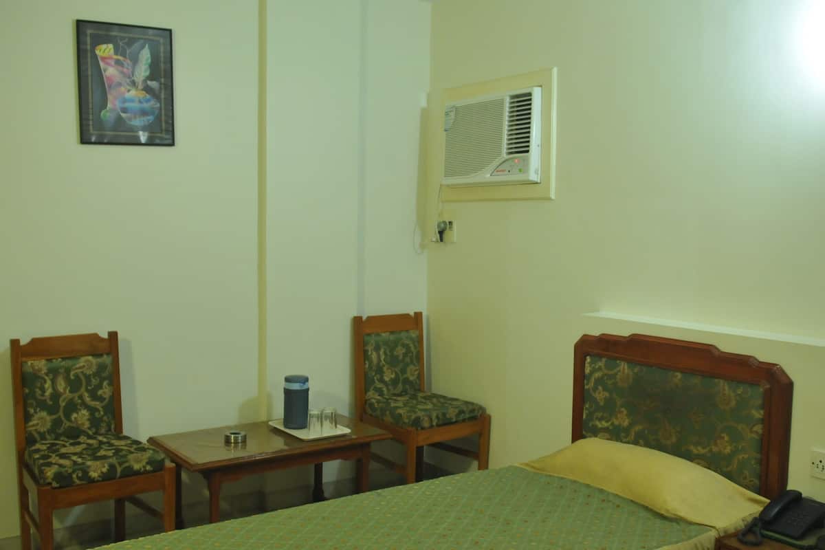A hotel room with a bed, two chairs, a small table, a wall-mounted air conditioner, and a framed picture.
