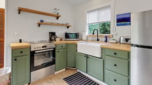 Una cocina con armarios verdes, un refrigerador de acero inoxidable, un microondas, una estufa y una ventana con persianas.