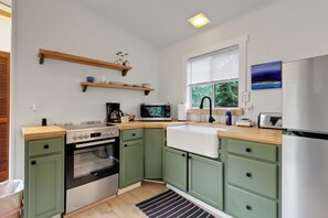 A kitchen with green cabinets, a stainless steel refrigerator, a microwave, a stove, and a window with blinds.