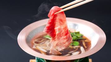 Un tazón de sopa con palillos levantando un trozo de carne, vapor elevándose del tazón y una base verde.