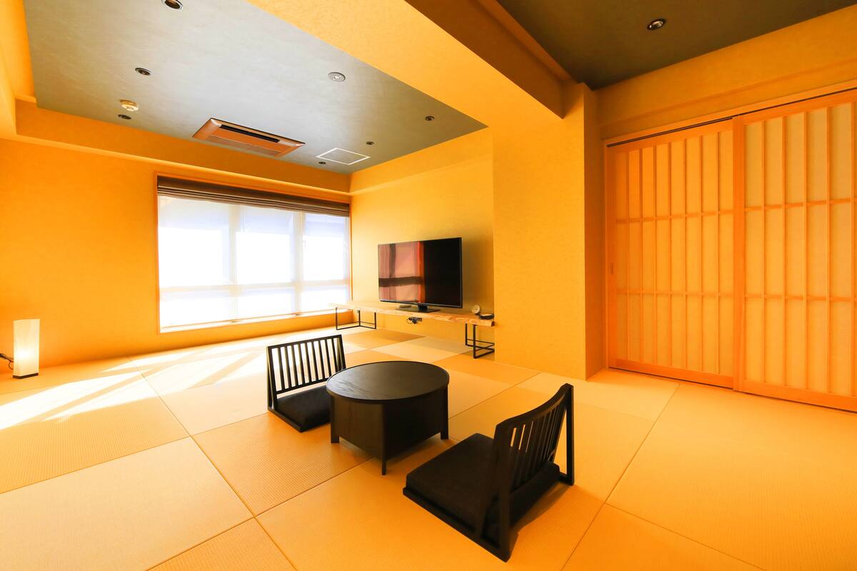 A room with tatami flooring, a tatami mat table, a sofa, a TV, and a sliding door.