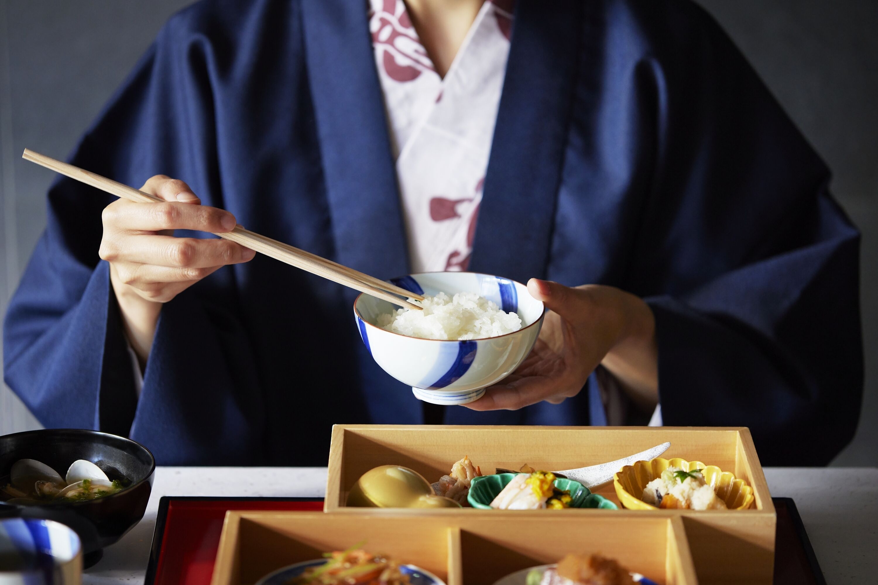 A person in traditional attire holding a bowl of rice with chopsticks.