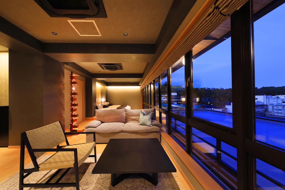 A modern living room with a sofa, a chair, and a coffee table. There is a large window with a view of the outside.