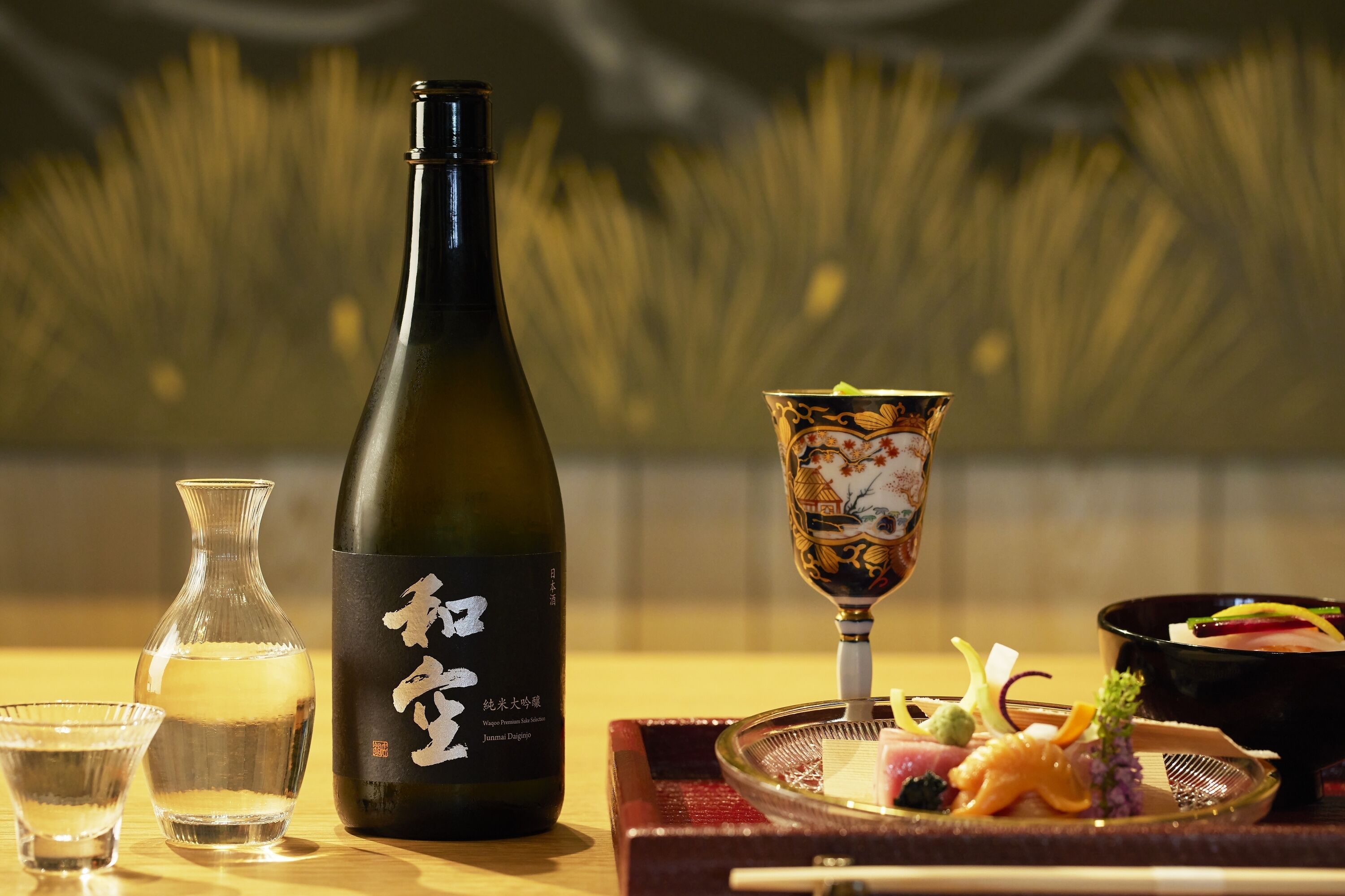 En sakeflaske, en lille vase og en traditionel japansk ret på et træbord.