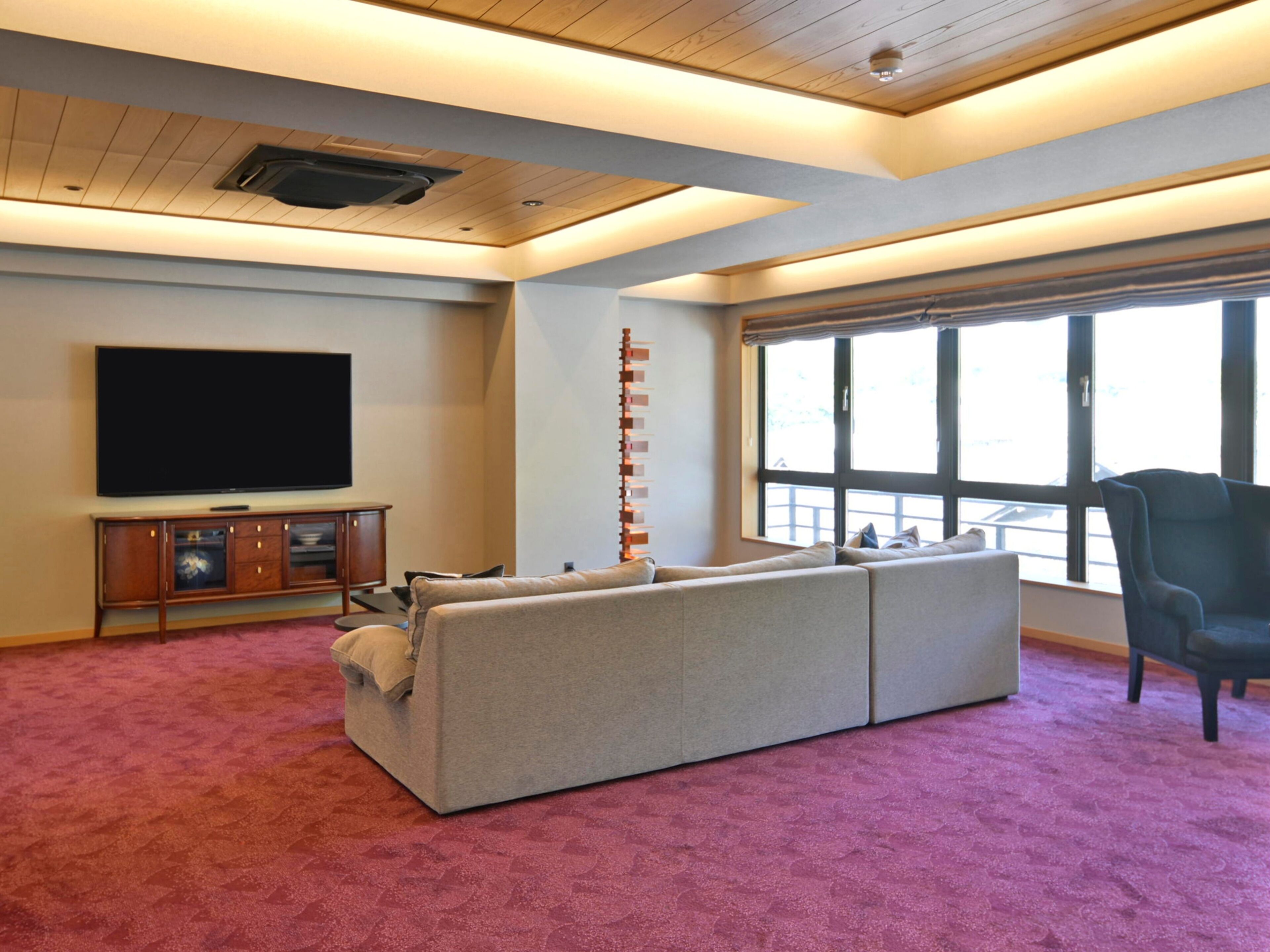 A living room with a large flat-screen TV, a sectional sofa, a tall red and white column, and a large window with a view.