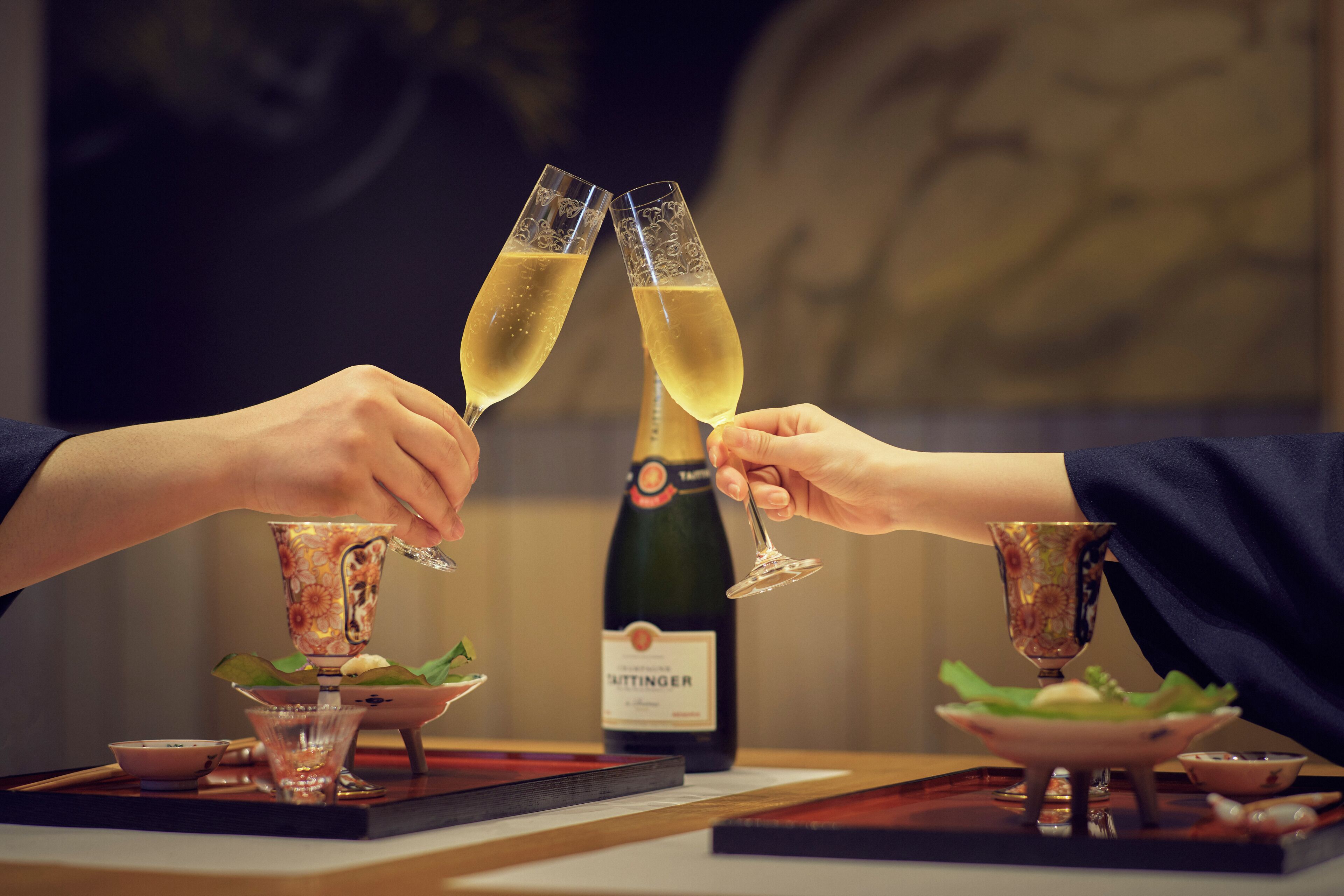 Dos personas brindando con copas de champán, una botella de vino y una decoración de mesa con estampado floral.