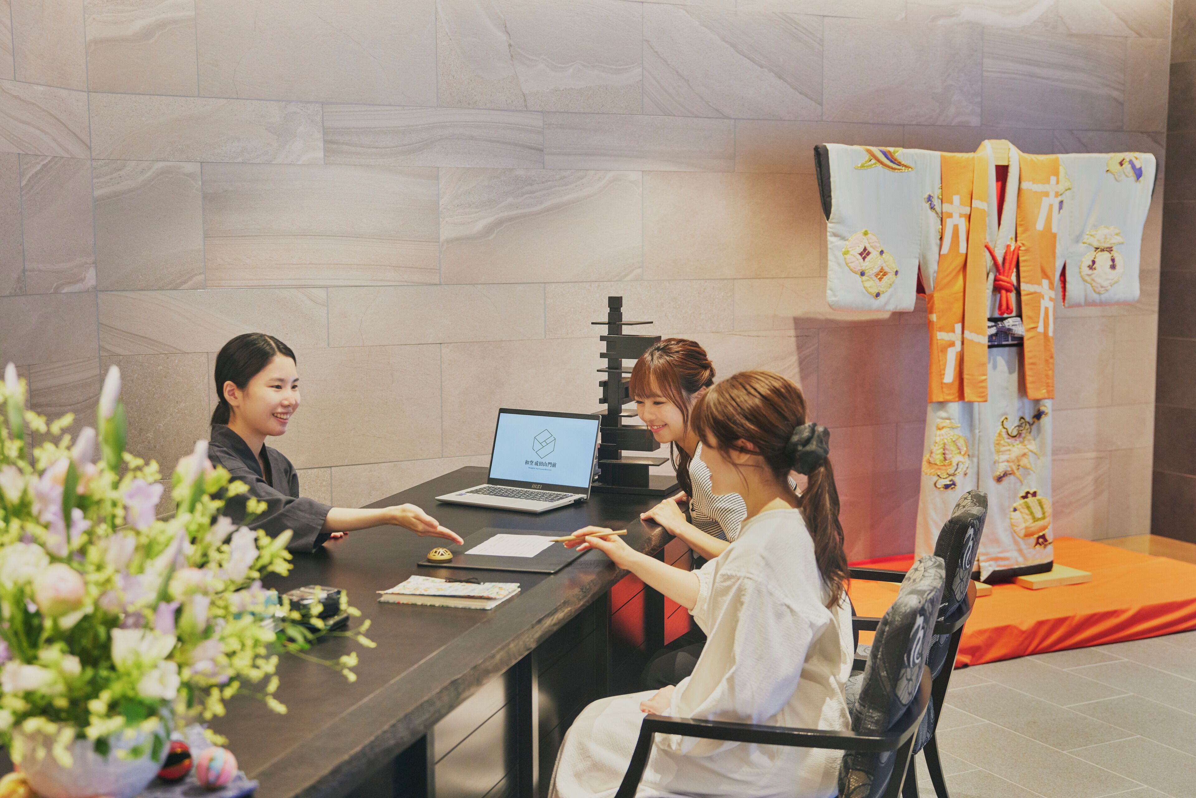 A reception desk with a laptop, documents, and a vase of flowers.