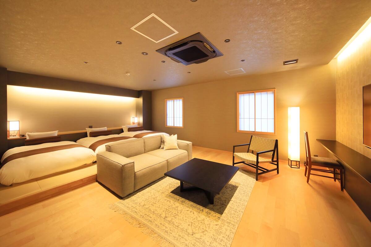 A modern hotel room with a sofa, two beds, a coffee table, and a TV.