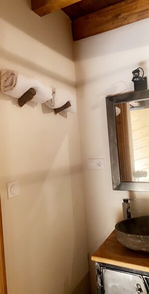 Ein Badezimmer mit Holzboden, einem Waschbecken mit runder Schüssel, einem Spiegel und einem Handtuchhalter mit zwei Handtüchern.