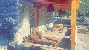 Un bâtiment en pierre doté d’une terrasse en bois, de deux bancs en bois et d’une pergola en bois.