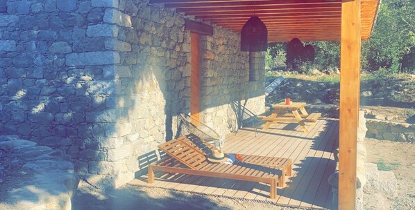 Ein Steingebäude mit einer Holzdielen-Terrasse, zwei Holzbanken und einer Holzpergola.