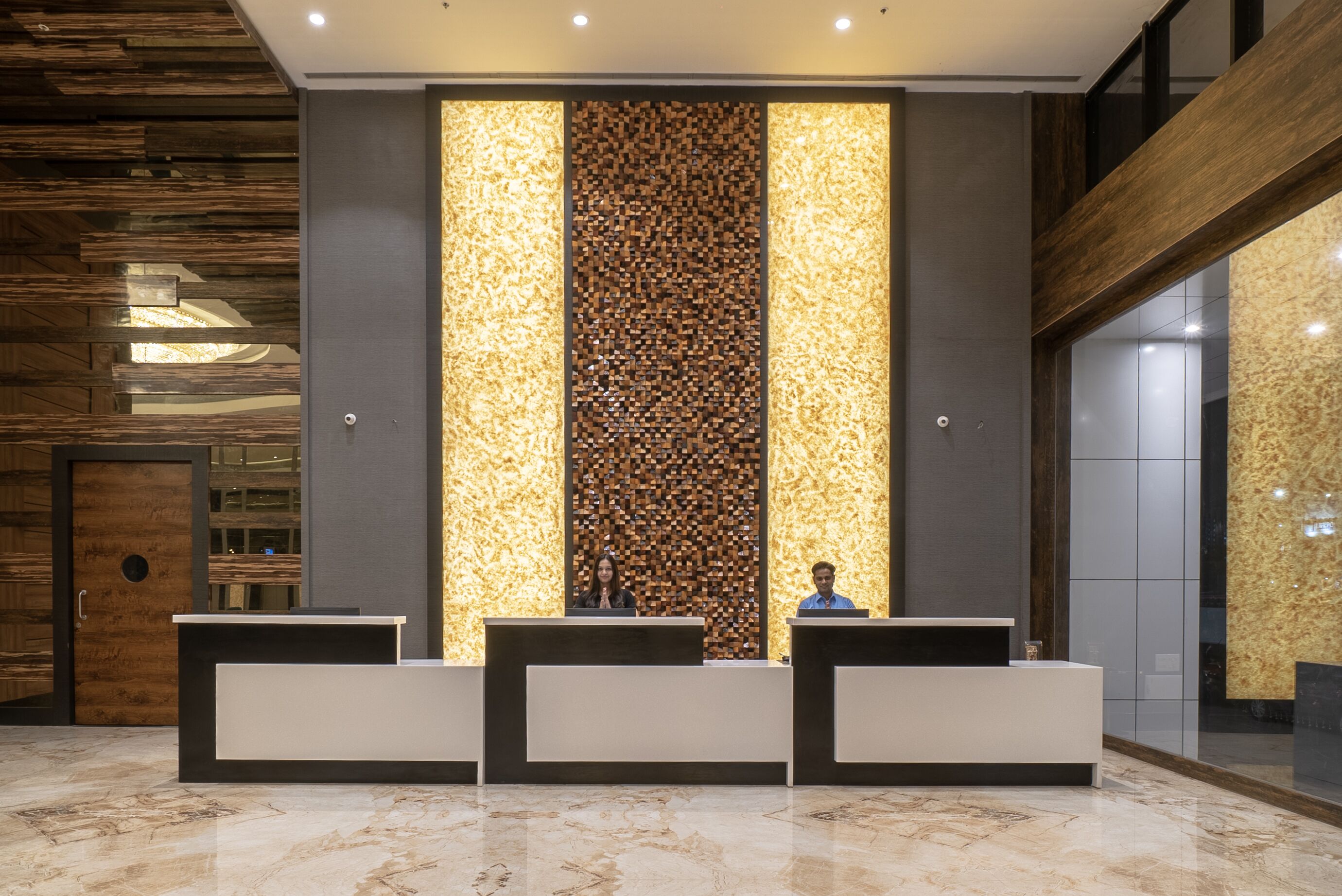 A reception area with three reception desks, a wooden wall with a vertical light panel, and a marble floor.